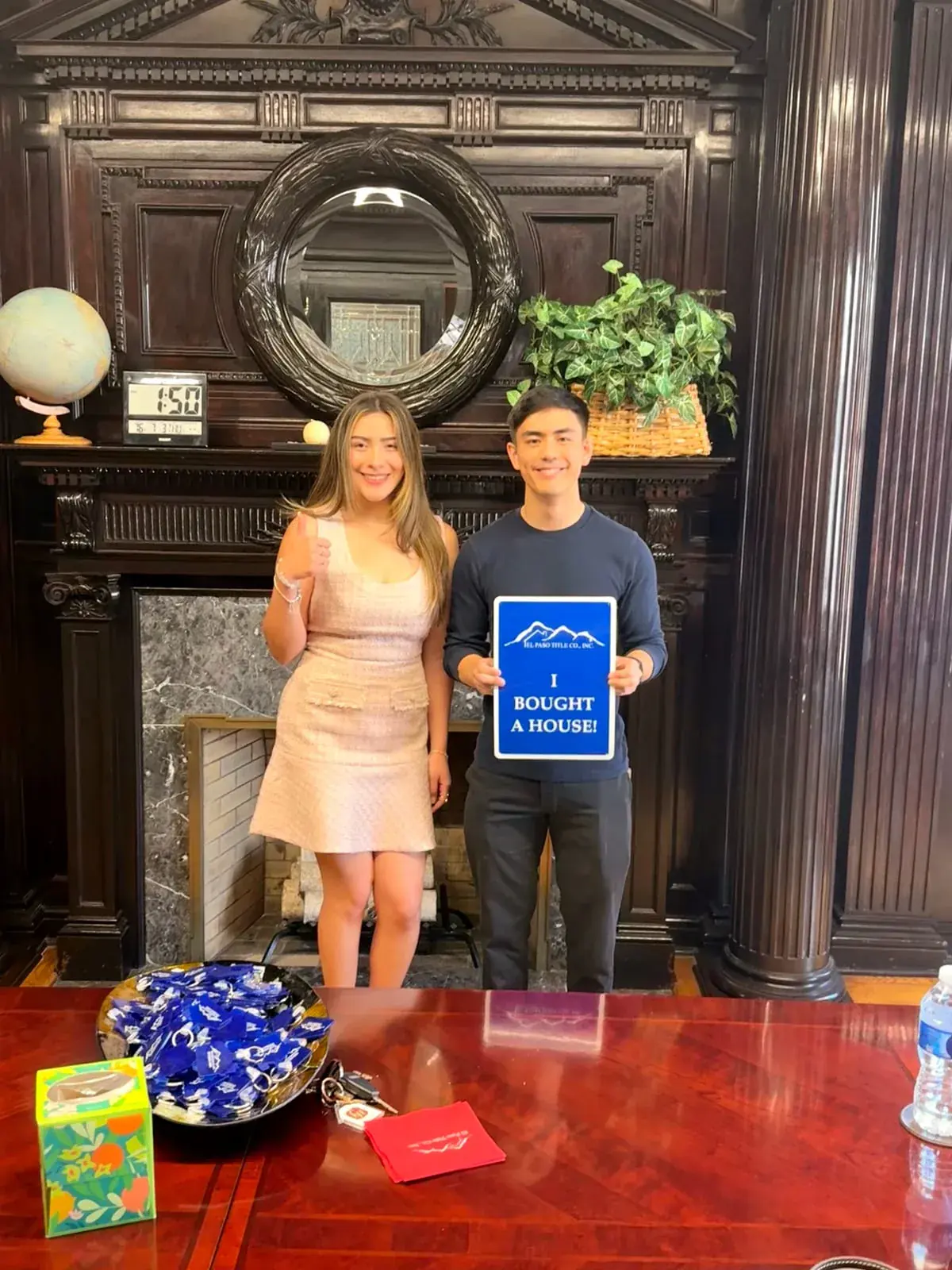 A client holding an “I bought a house!” sign next to Ximena Martinez, who gives a thumbs up